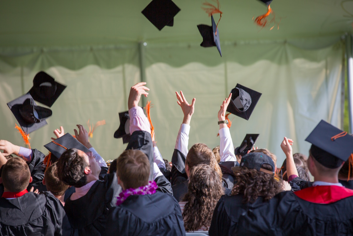 A crowd of young graduates toss their hats into the air in celebration.