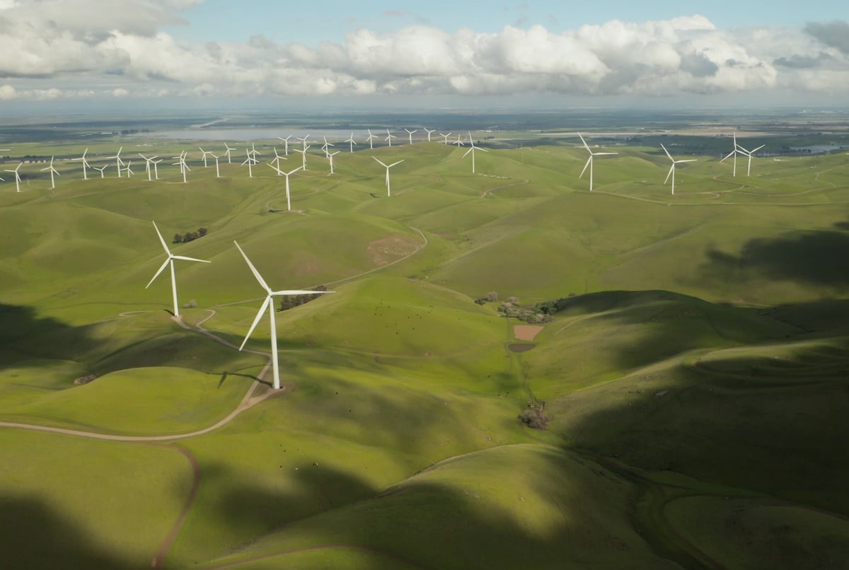 Rolling, green hills dotted with sleek windmills against a partly cloudy skyline.