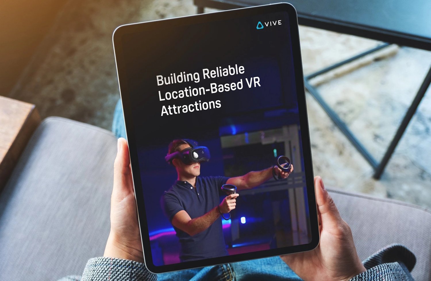 Hands hold a mobile tablet with the screen displaying the cover page of HTC Vive's report, Building Reliable Location-Based VR Attractions.